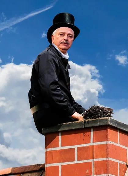 Ein Rauchfangkehrmeister mit der typischen schwarzen Kleidung und dem Zylinder auf einem Schornstein.